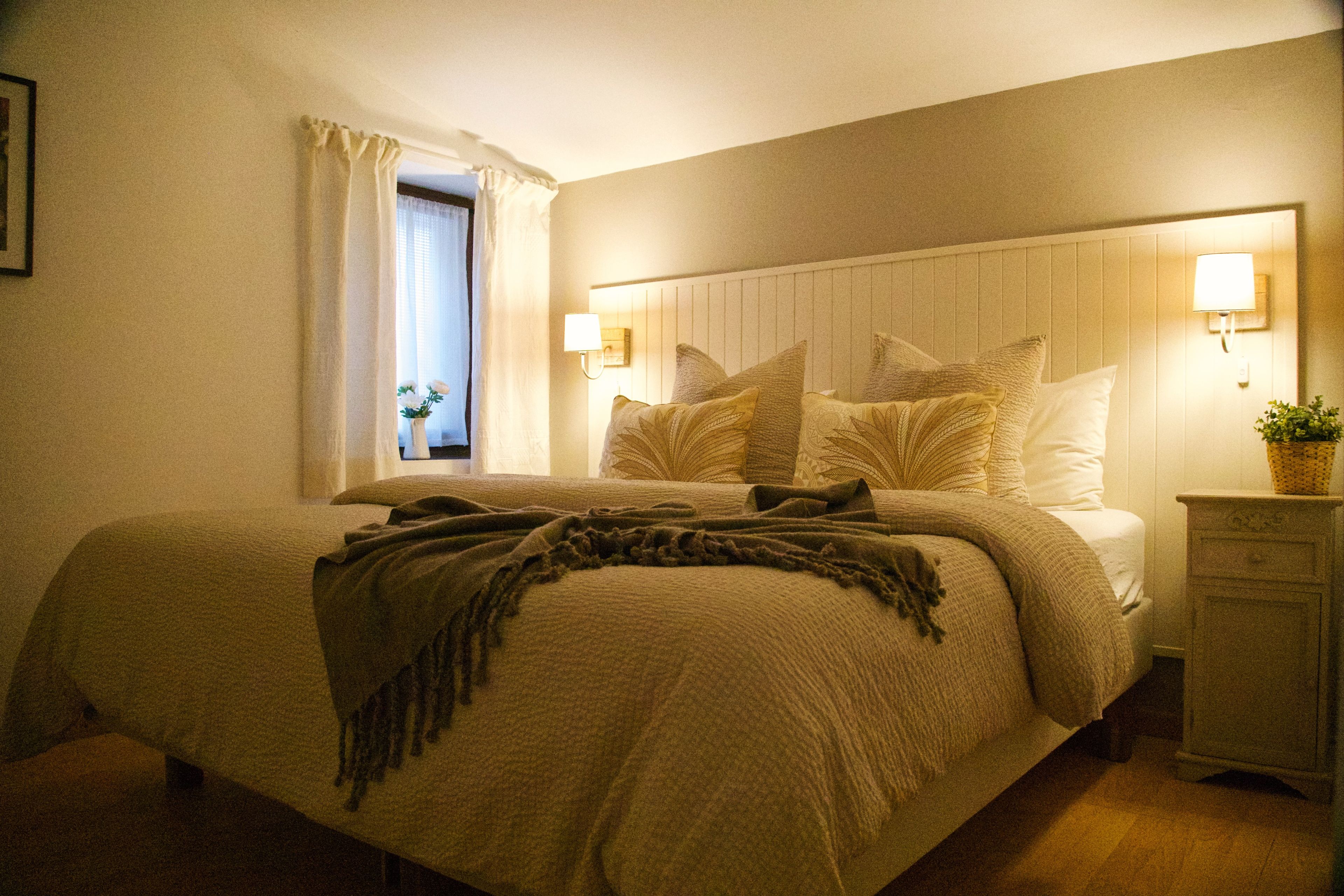 A bedroom with a bed, bedside lamps, a nightstand, and a window with curtains.
