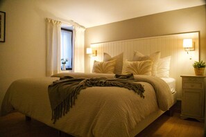A bedroom with a bed, bedside lamps, a nightstand, and a window with curtains.