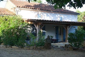 A traditional house with a tiled roof, a covered porch, and a stone statue in front. - Secluded Gite, private garden, large heated pool, tranquil setting (Cuzorn)