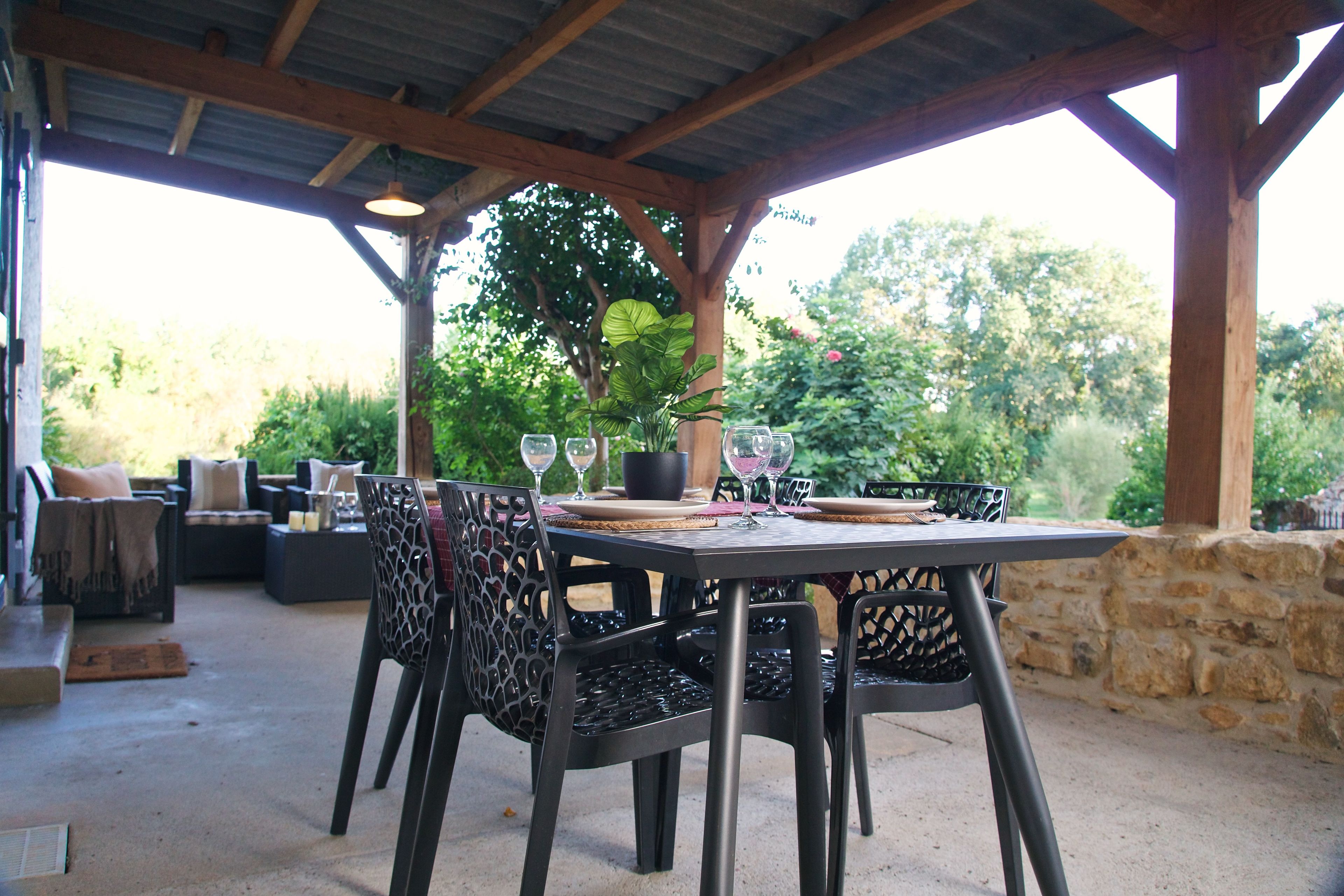 An outdoor patio with a table set for dining, surrounded by chairs, and a potted plant.