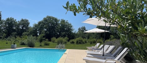 A swimming pool with lounge chairs and umbrellas, surrounded by greenery.