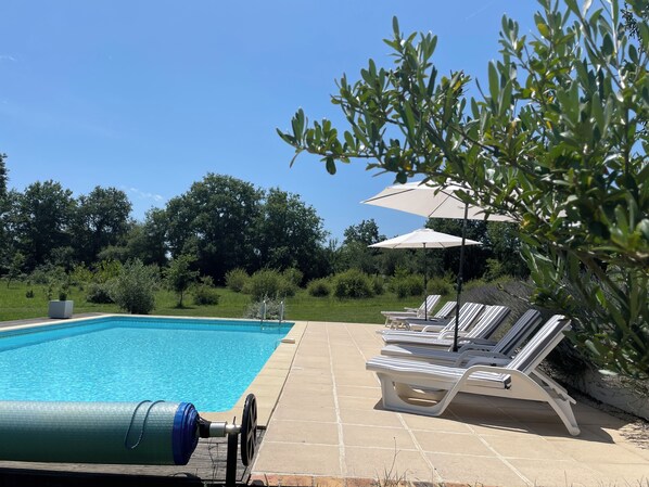 Una piscina con sillas de descanso y sombrillas, rodeada de vegetación.