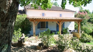 A traditional house with a tiled roof, a covered patio with outdoor furniture, and a garden with various plants.
