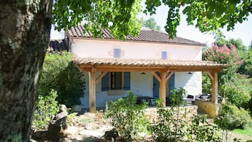 Ein traditionelles Haus mit Ziegeldach, einer überdachten Terrasse mit Gartenmöbeln und einem Garten mit verschiedenen Pflanzen.