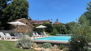 A pool area with lounge chairs and umbrellas, surrounded by greenery and stone walls.