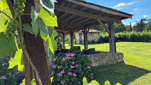 A rustic outdoor seating area with a stone wall backdrop, a pergola, and a grassy lawn.