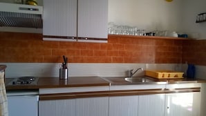 Una cocina con estufa, lavamanos y armarios. Hay utensilios en un organizador y un recipiente amarillo sobre la encimera.