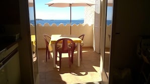 Un patio exterior con mesa y sillas, un paraguas blanco y vista al mar.