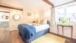 A bedroom with a bed, a bedside table with a vase of flowers, a window with curtains, and a wooden floor. - Stables at Valley Farm Barns, Snape (Saxmundham)