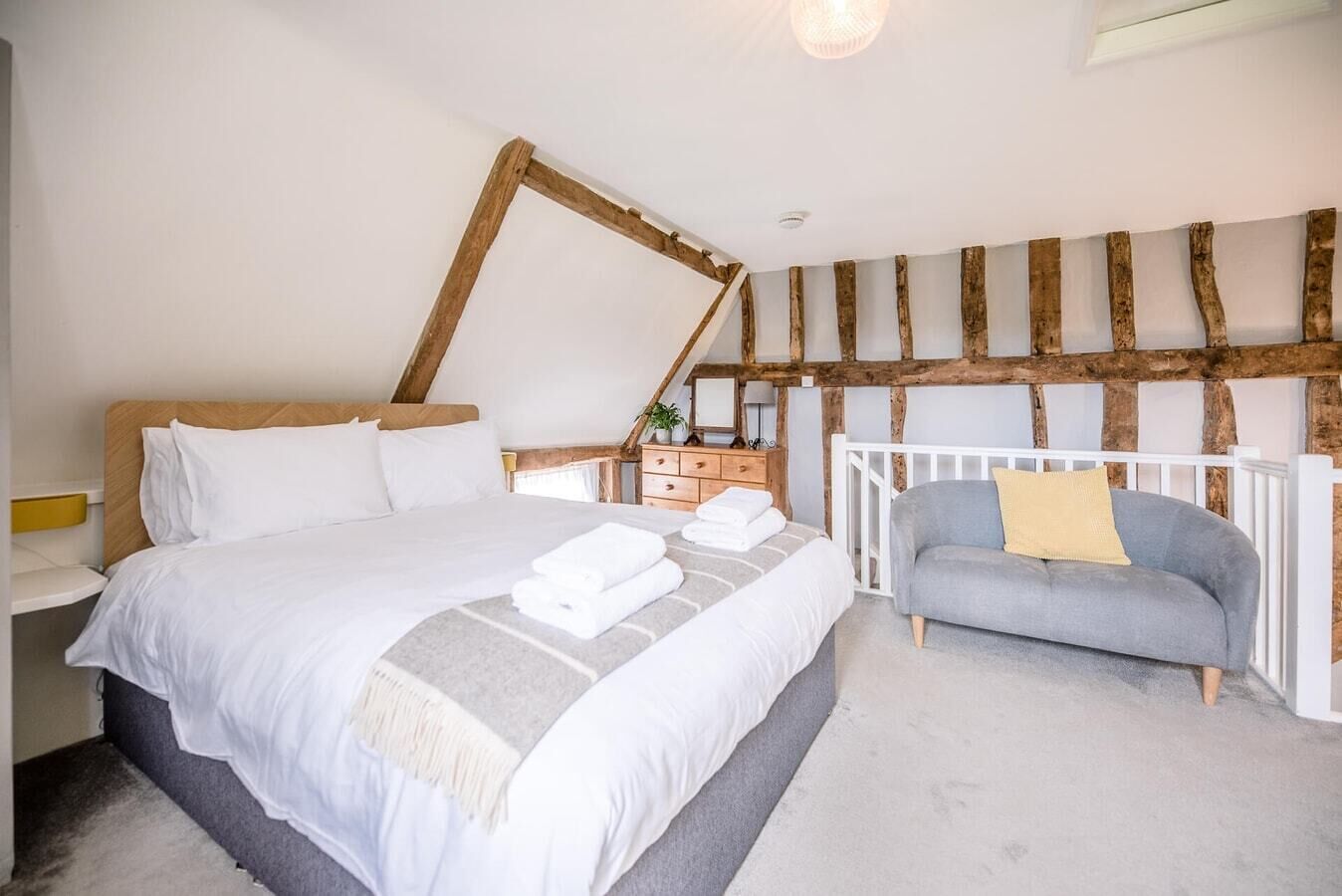 A bedroom with a large bed, a grey sofa, and a wooden ceiling.