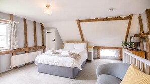 A bedroom with a large bed, a chair, a bedside table, and a window with curtains. - Hayloft at Valley Farm Barns, Snape (Saxmundham)