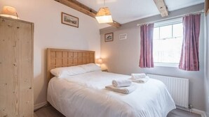 A bedroom with a wooden headboard bed, white linens, a window with curtains, and a radiator. - Suncatch Corner, Saxmundham (Saxmundham)