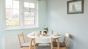 A dining area with a round table, four chairs, and a window with a view of buildings. - Suncatch Corner, Saxmundham (Saxmundham)