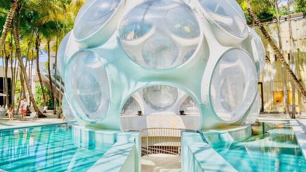 A spherical structure with transparent sections over a pool, surrounded by palm trees. - Modern Rustic 1Bdrm Condo W/Bay & Pool Views (Miami)