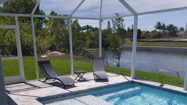 A covered swimming pool with two lounge chairs and a small table, surrounded by a white pergola and a view of a lake and greenery. -  Cape Coral FL Escape! 4Bd, Private pool, waterfront view! Close to beaches



 (Cape Coral)