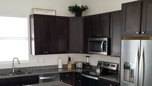 A modern kitchen with dark cabinets, stainless steel appliances, a granite countertop, and a bar stool. -  Cape Coral FL Escape! 4Bd, Private pool, waterfront view! Close to beaches



 (Cape Coral)