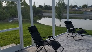A covered outdoor area with two black lounge chairs and a view of a body of water and greenery. -  Cape Coral FL Escape! 4Bd, Private pool, waterfront view! Close to beaches



 (Cape Coral)