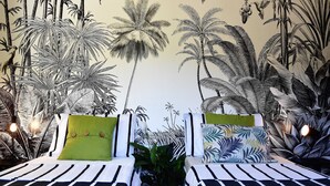 A room with two beds, each with black and white striped bedding, a large mural of tropical foliage on the wall, and a potted plant in the center.
