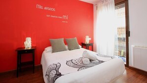 Un dormitorio con pared roja, una cama con ropa de cama estampada, dos mesitas de noche con lámparas y una ventana con cortinas.