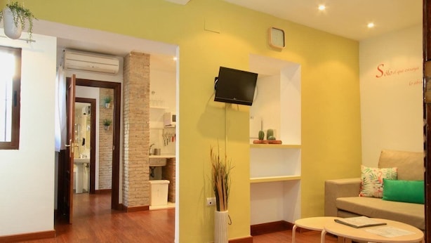 Habitación de hotel con suelo de madera, televisor montado en la pared, sofá con cojines y una mesita.