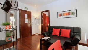 Una sala de estar moderna con un sofá de cuero negro, cojines rojos, una mesa de centro y un televisor montado en la pared.