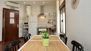 Cocina compacta con armarios blancos, estufa y microondas. Hay una mesa de comedor con sillas y una planta verde en el centro.