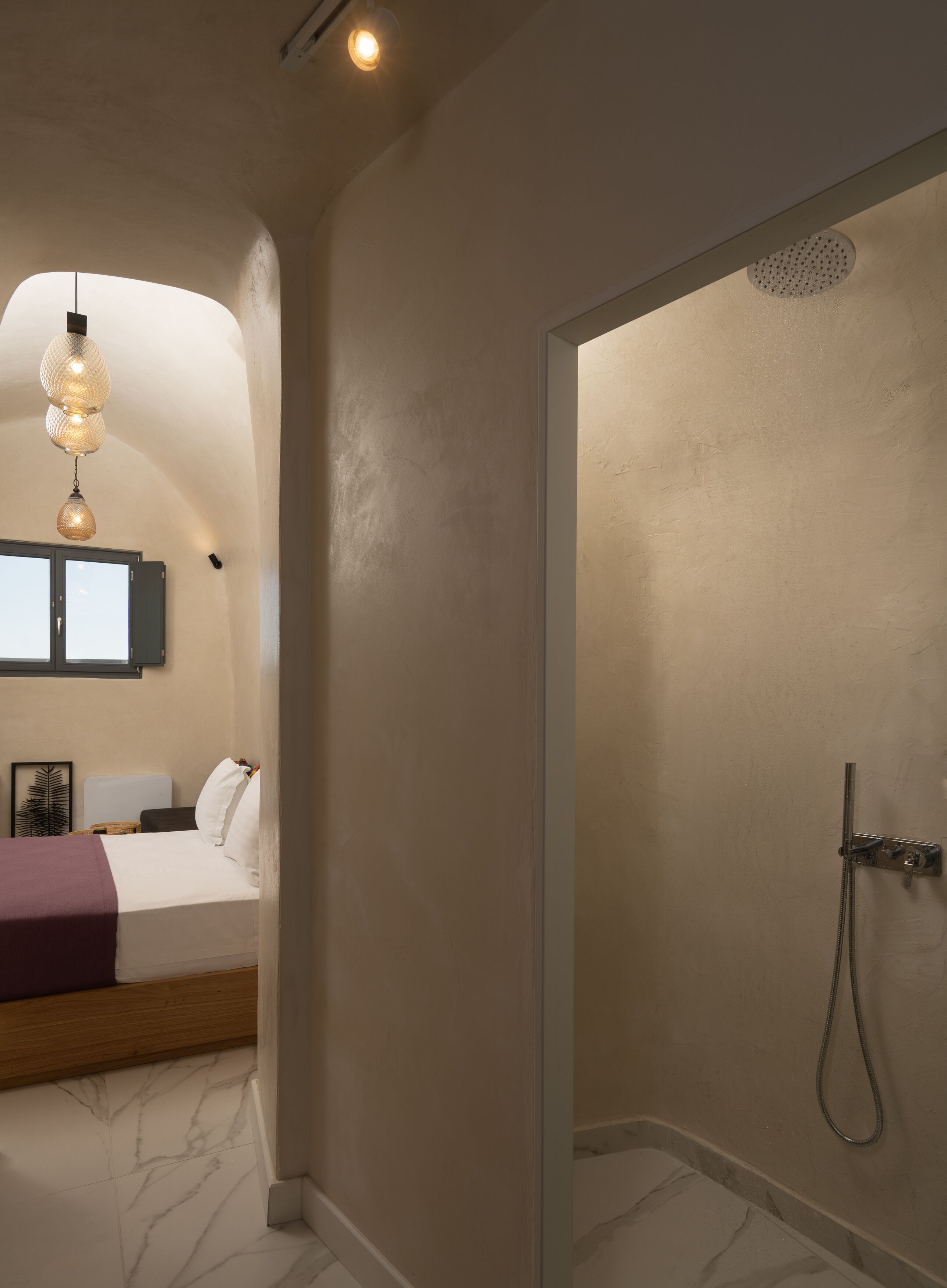Ein Schlafzimmer mit Bett, Nachttisch, einer Pendelleuchte und einem Duschbereich mit Handbrause.