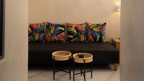 Un coin salon accueillant avec un canapé et deux fauteuils en osier, une porte en arc de cercle et un luminaire fixé au mur.