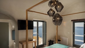 Une chambre avec un lit, un bureau, une chaise, une télévision et un balcon donnant sur la mer.