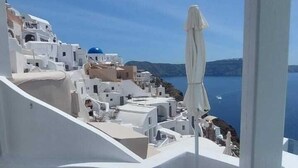 Un balcon avec une table et des chaises, donnant sur une ville côtière aux bâtiments blancs et sous un ciel bleu azur.