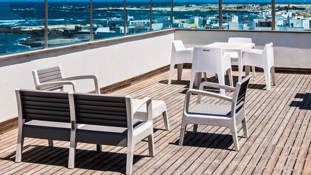 Eine Dachterrasse mit einer Holzterrasse, weißen Plastikstühlen und einer schwarz-weißen Bank.