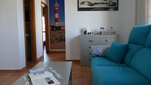Ein Wohnzimmer mit einem blauen Sofa, einem Couchtisch mit einem Buch und Dekorationselementen, einer grauen Kommode und einem gerahmten Bild eines Leuchtturms an der Wand.