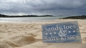 Ein Strand mit einem Schild, auf dem steht 'Sandy toes Salty kisses', und ein bewölkter Himmel.