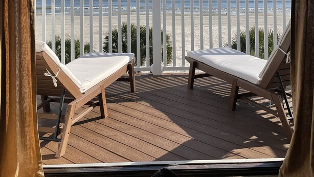 Una terraza de madera con dos sillones blancos frente a la playa.