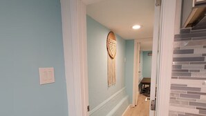 A hallway with light blue walls, a wooden floor, and a dreamcatcher decoration.