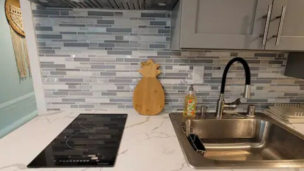 A kitchen with a modern design, featuring a stainless steel sink, a built-in oven, and a backsplash with a mosaic tile pattern.