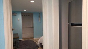A hallway with a wooden floor, a dark rug, and a refrigerator on the right.
