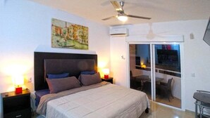 Ein Schlafzimmer mit einem Bett, Nachttischen, einem Deckenventilator und einer Glastür, die auf einen Balkon führt.