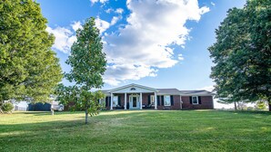 A two-story house with a front porch, surrounded by a well-maintained lawn and large trees.