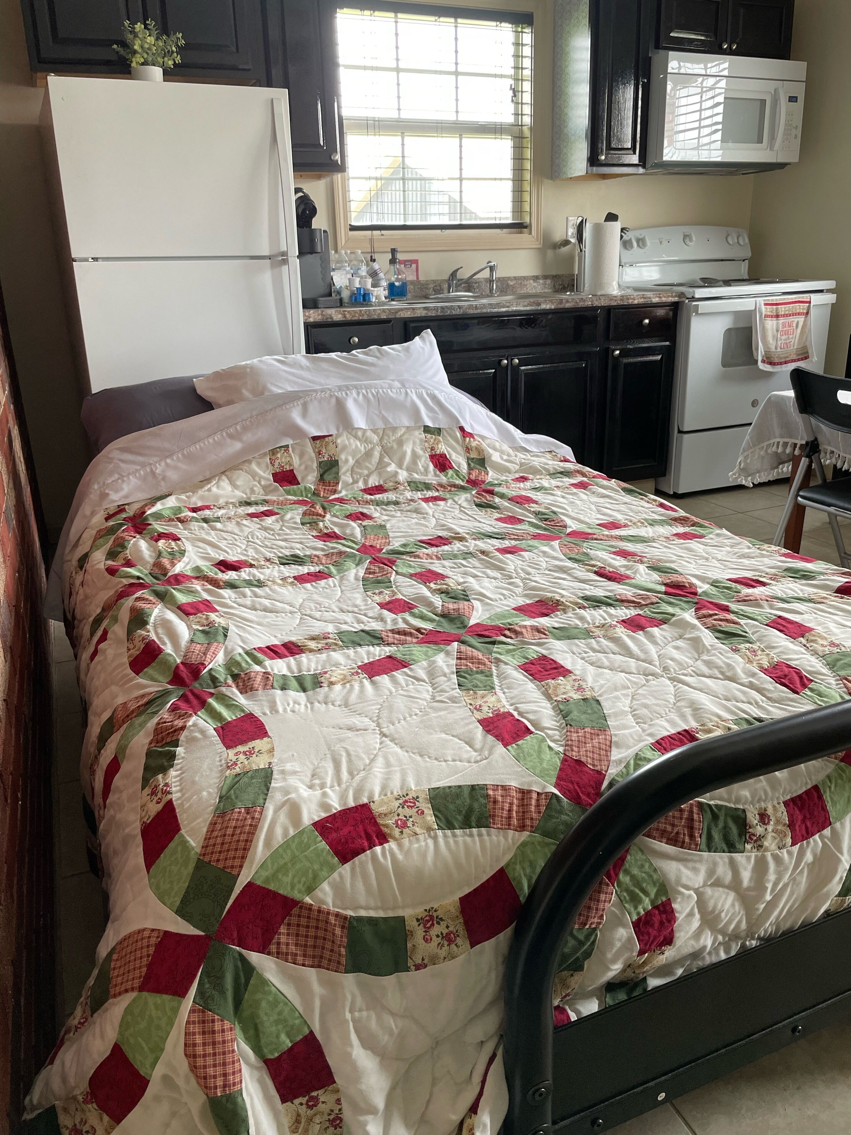 A bedroom with a bed, a window, a kitchenette, and a refrigerator.