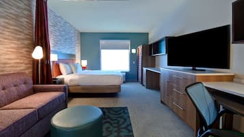 A hotel room with a bed, a sofa, a desk, a TV, and a window.