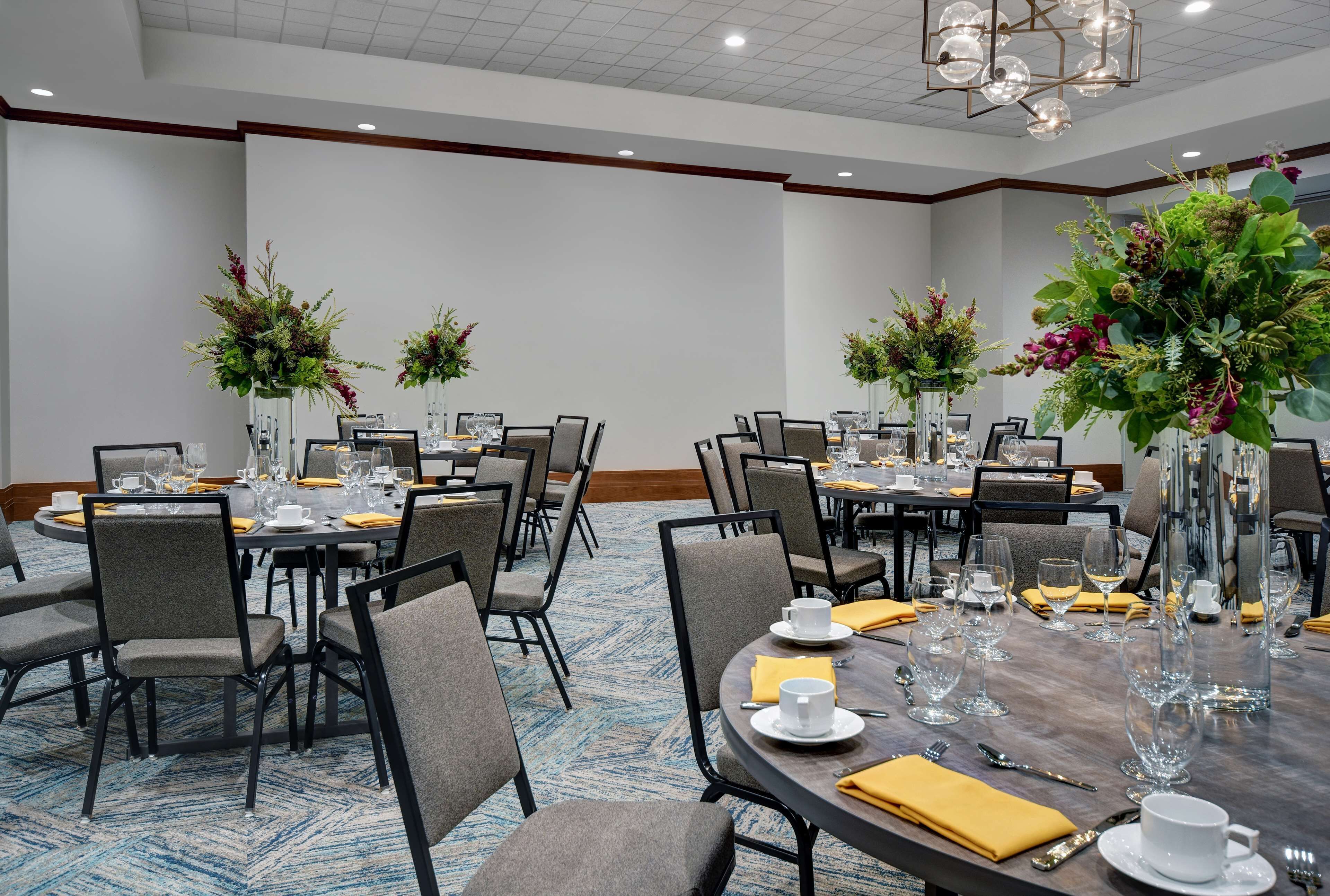 A conference room with round tables, chairs, and floral centerpieces.