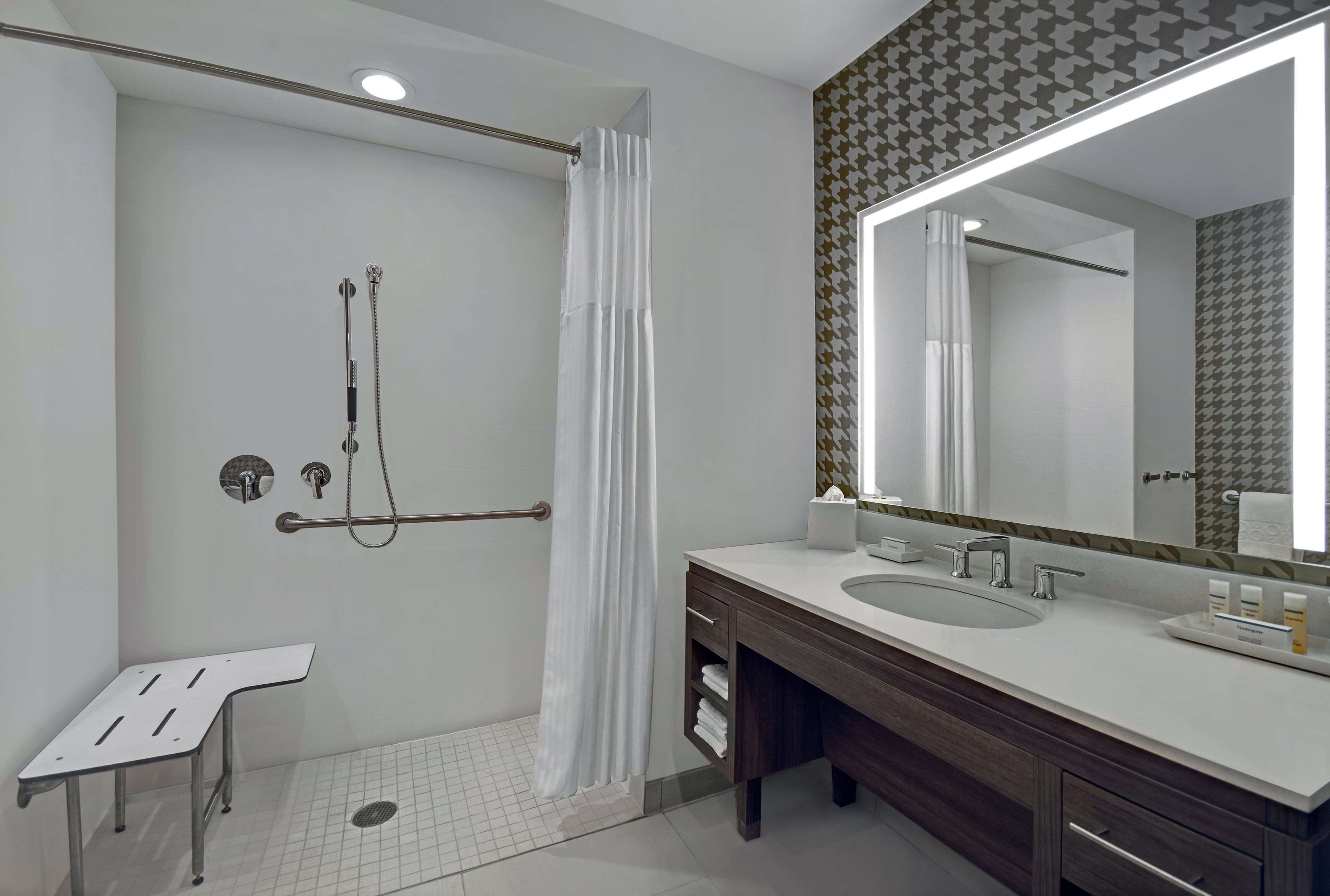 A modern bathroom with a shower, grab bar, and a large mirror.