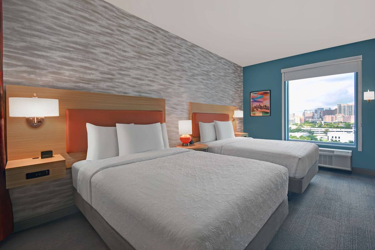 A hotel room with two beds, a city view, and a textured wall.