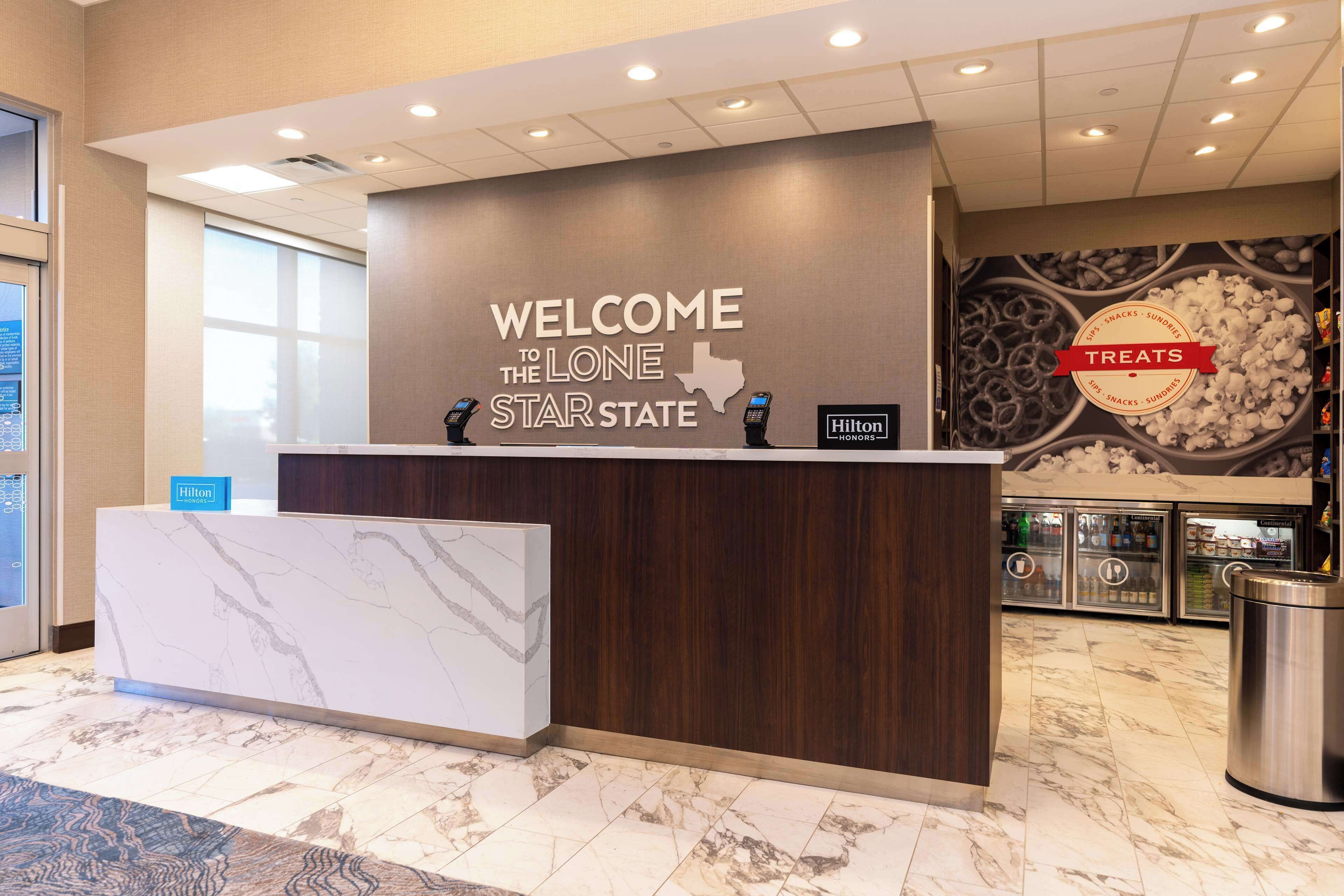 A hotel reception desk with a marble counter, a wooden panel, and a sign that reads "WELCOME TO THE LONE STAR STATE TREATS".