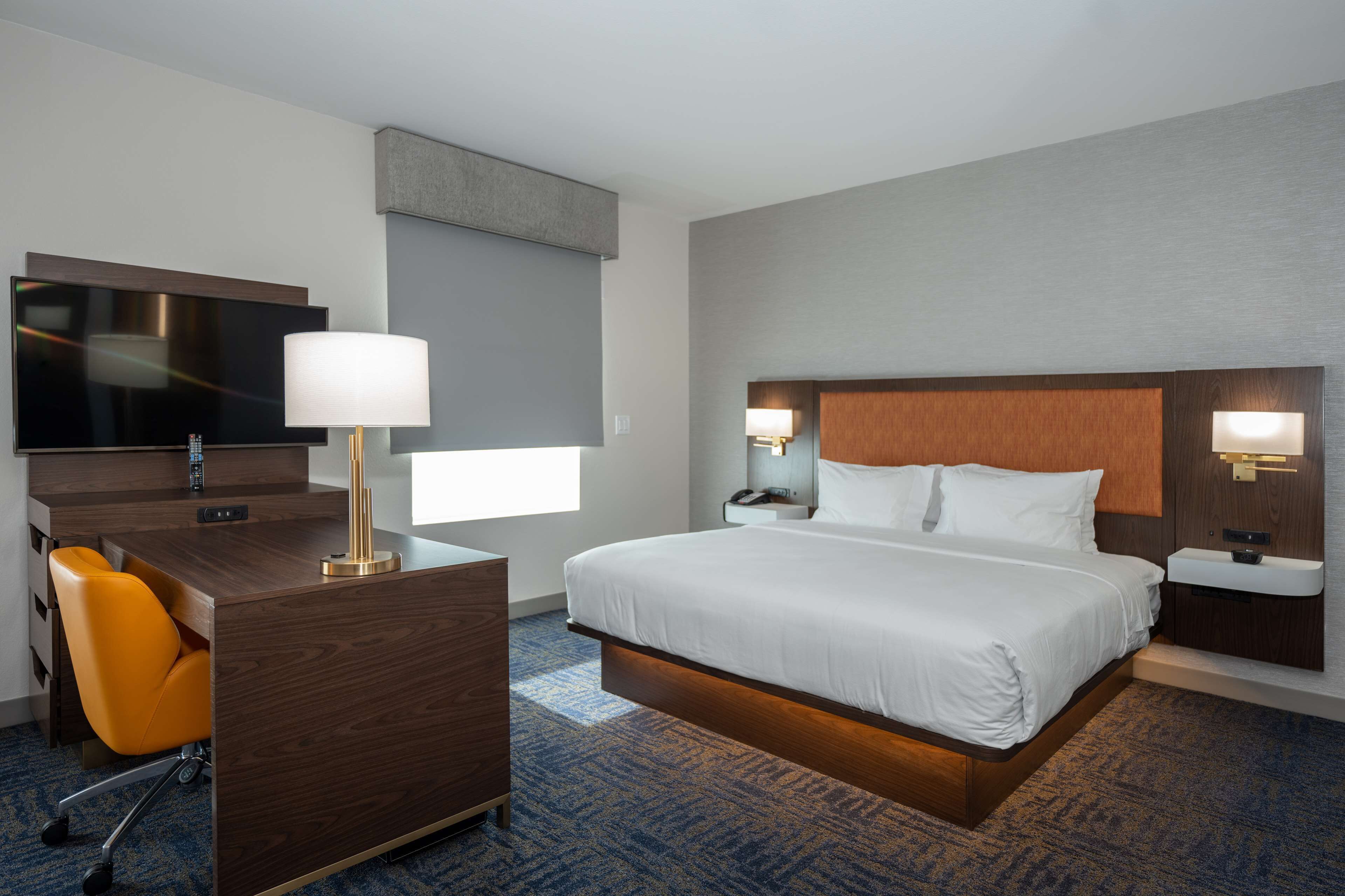 Une chambre d’hôtel moderne dotée d’un grand lit, d’un bureau avec une chaise, d’une télévision et d’une salle de bain avec un lavabo et un miroir.