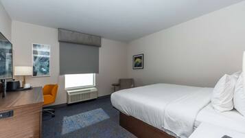 A hotel room with a bed, a desk, a chair, a window, and artwork on the walls.