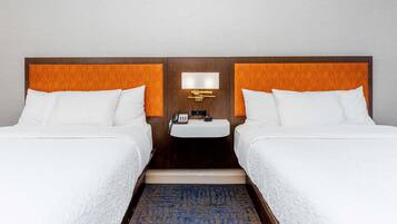 A hotel room with two beds, a nightstand with a lamp, and a blue patterned rug.