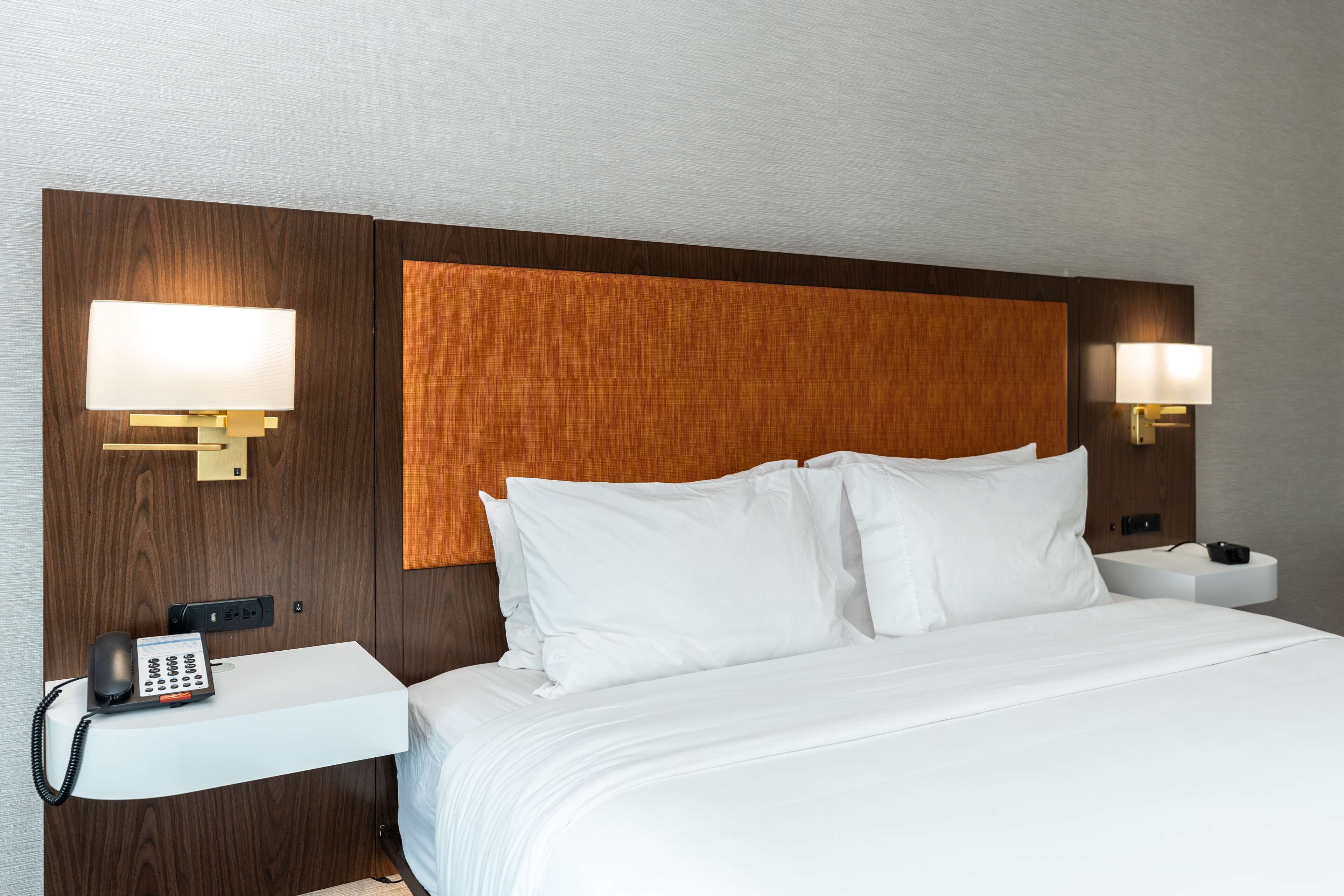 A hotel room with a large bed, two bedside tables, a phone, and wall-mounted lamps.
