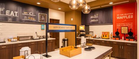 Un espace moderne dédié au petit-déjeuner, avec un panneau indiquant que le service commence ici, une machine à café et un présentoir à gaufres.